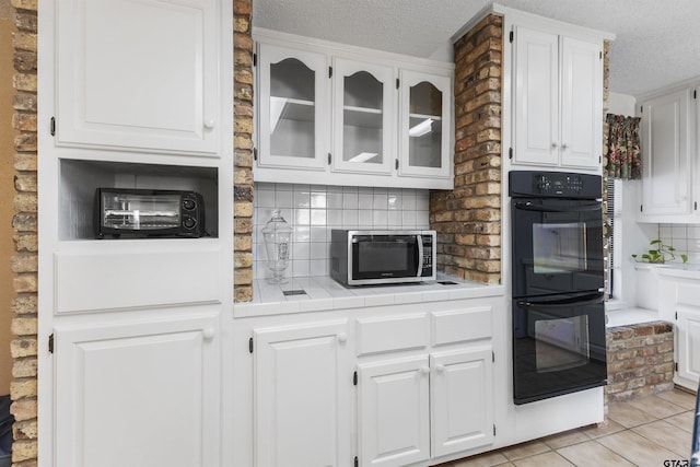 kitchen featuring light tile patterned floors, white cabinetry, black double oven, tile counters, and a textured ceiling