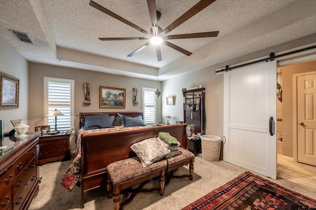 bedroom with a raised ceiling, a textured ceiling, ceiling fan, and a barn door