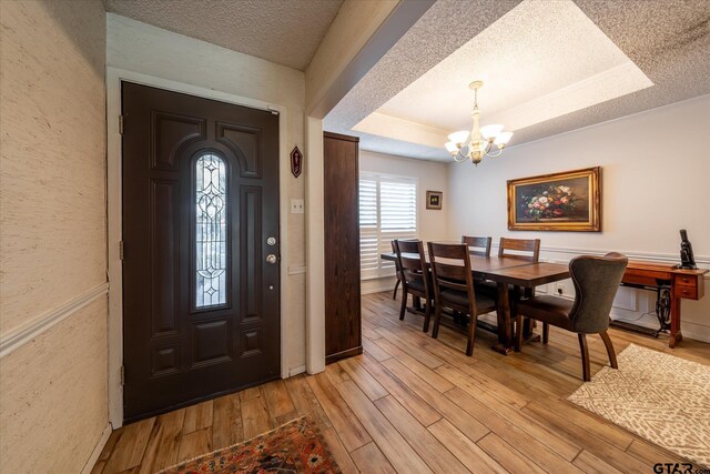 entryway with a notable chandelier, light hardwood / wood-style flooring, a raised ceiling, and a textured ceiling