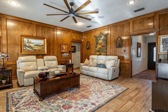 living room with light hardwood / wood-style floors, ceiling fan, wood walls, and a textured ceiling