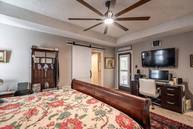 bedroom with a textured ceiling, a raised ceiling, a barn door, carpet, and ceiling fan