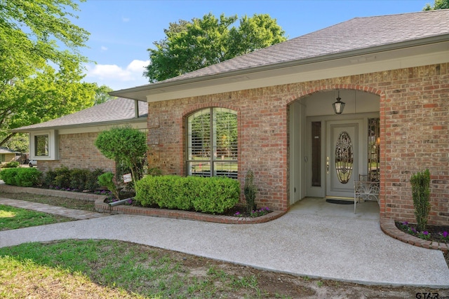 view of exterior entry with brick siding and a shingled roof