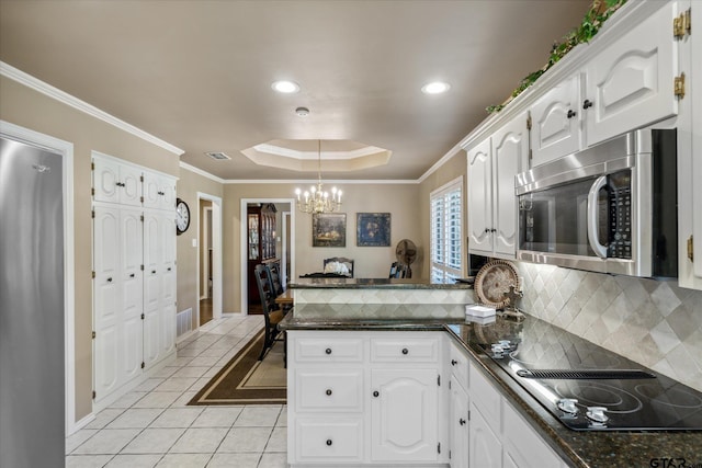 kitchen featuring a raised ceiling, an inviting chandelier, a peninsula, stainless steel microwave, and white cabinetry
