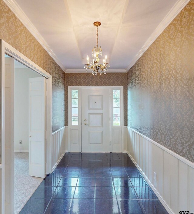 carpeted foyer entrance with ornamental molding and a chandelier