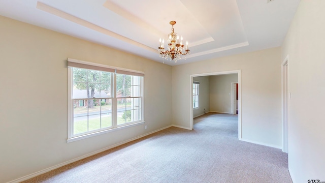 empty room featuring light colored carpet, a chandelier, and a raised ceiling