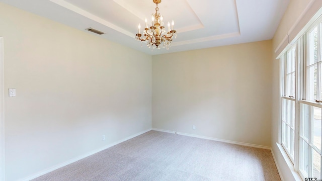 carpeted spare room with a notable chandelier and a raised ceiling