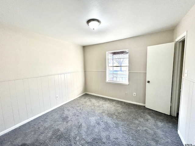 carpeted spare room featuring a wainscoted wall