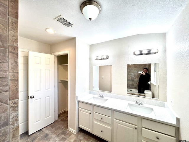 bathroom with double vanity, visible vents, a sink, and tiled shower