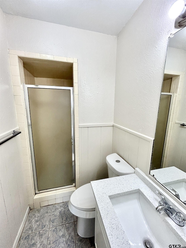 full bath featuring a stall shower, toilet, a wainscoted wall, tile patterned floors, and vanity