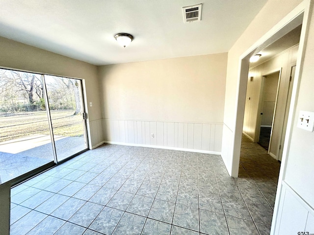 empty room featuring tile patterned flooring, visible vents, and wainscoting