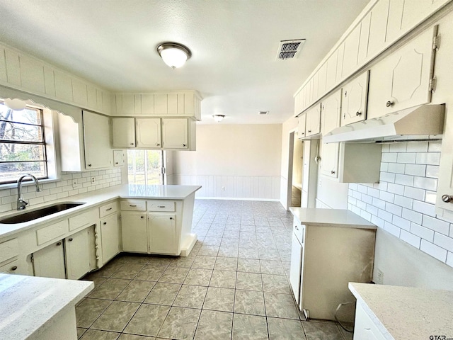 kitchen featuring visible vents, wainscoting, a peninsula, light countertops, and a sink