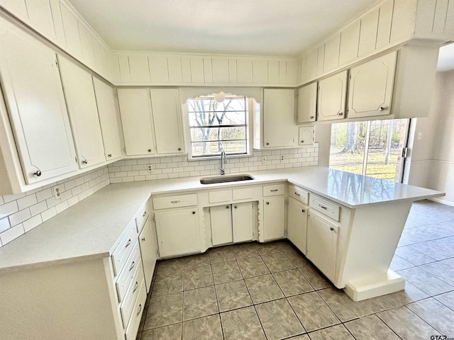 kitchen featuring light tile patterned floors, a peninsula, a sink, light countertops, and decorative backsplash