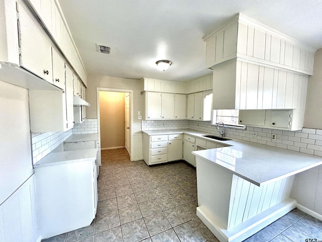 kitchen with light countertops, visible vents, backsplash, a sink, and a peninsula