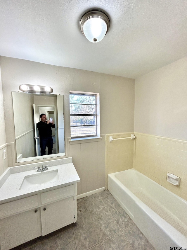 full bathroom featuring a tub to relax in, wainscoting, a textured ceiling, vanity, and tile patterned floors