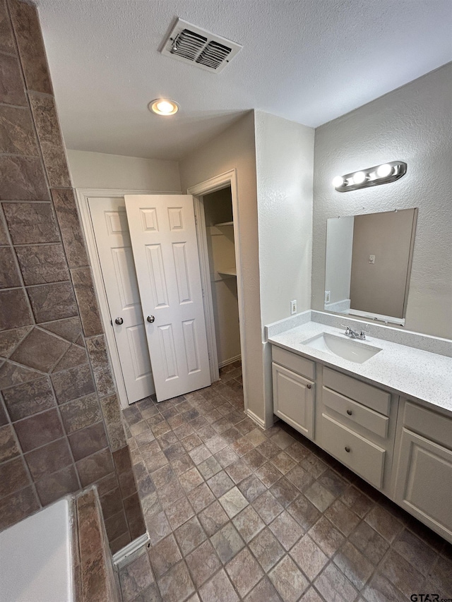 bathroom featuring a textured ceiling, a textured wall, vanity, visible vents, and stone finish floor