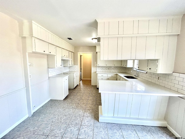 kitchen featuring visible vents, decorative backsplash, a peninsula, under cabinet range hood, and a sink