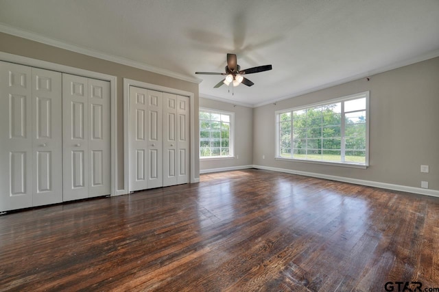 unfurnished bedroom with ceiling fan, dark wood-type flooring, two closets, and ornamental molding