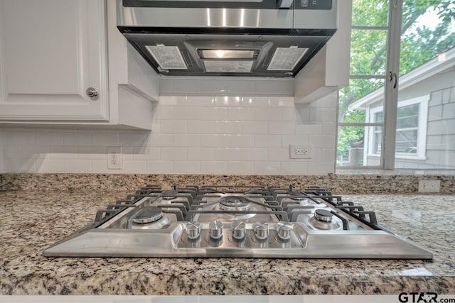 details featuring white cabinetry, light stone countertops, stainless steel gas cooktop, ventilation hood, and decorative backsplash