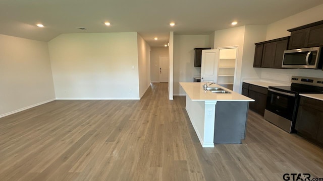 kitchen featuring stainless steel appliances, an island with sink, sink, and light wood-type flooring