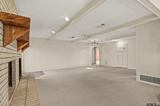 unfurnished living room featuring beam ceiling, ceiling fan, a textured ceiling, and a brick fireplace