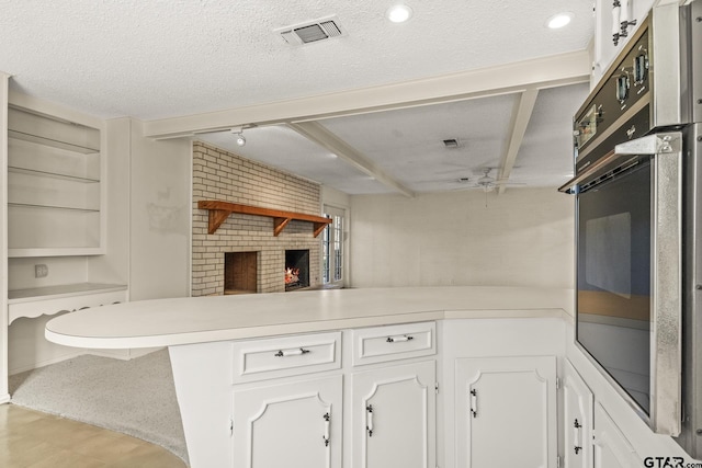 kitchen with kitchen peninsula, a fireplace, a textured ceiling, white cabinets, and black oven