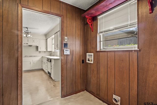 interior space with dishwasher, wood walls, white cabinetry, and a textured ceiling