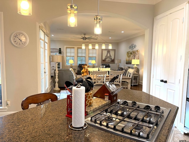 kitchen with ornamental molding, hanging light fixtures, dark stone countertops, stainless steel gas cooktop, and ceiling fan