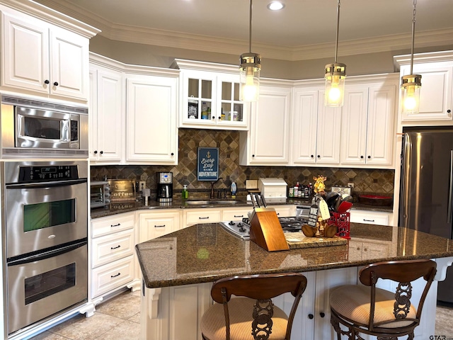 kitchen with ornamental molding, dark stone counters, a kitchen bar, a center island, and white cabinets