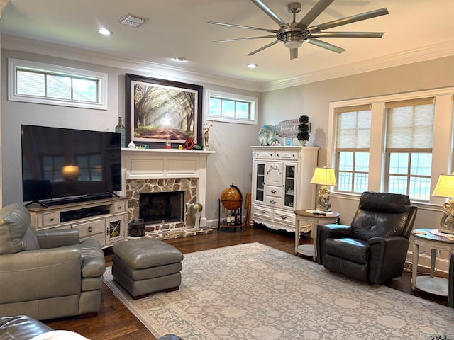 living room featuring a stone fireplace, ceiling fan, hardwood / wood-style flooring, and ornamental molding