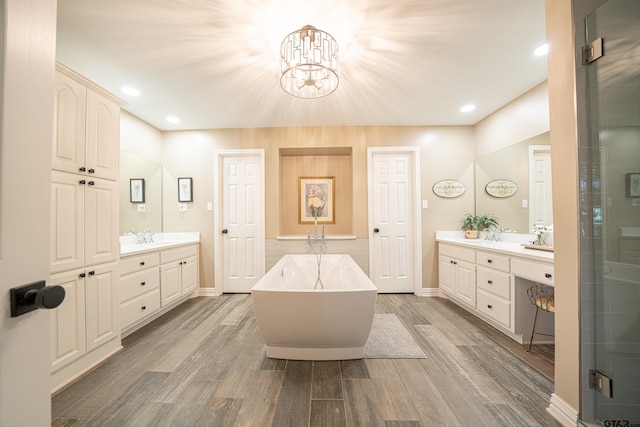 full bath featuring a stall shower, a freestanding bath, two vanities, and wood finished floors