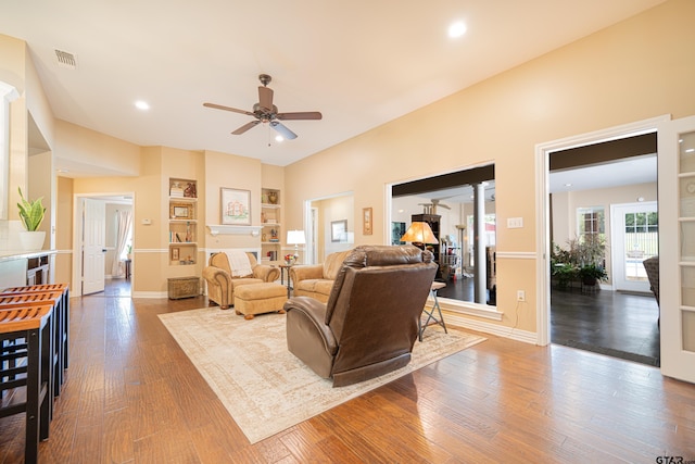 living room featuring ceiling fan, wood finished floors, visible vents, baseboards, and ornate columns