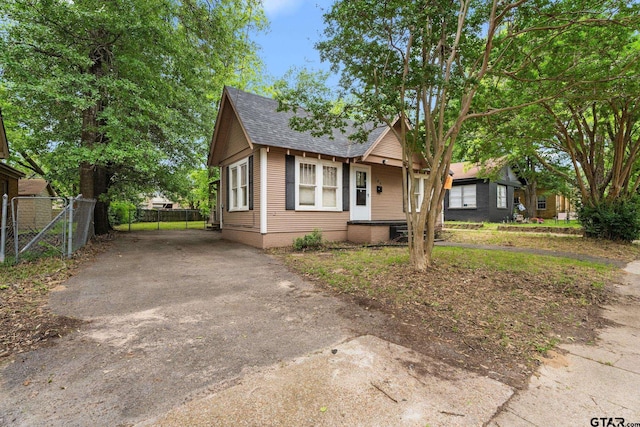 bungalow-style home with a shingled roof, fence, and driveway