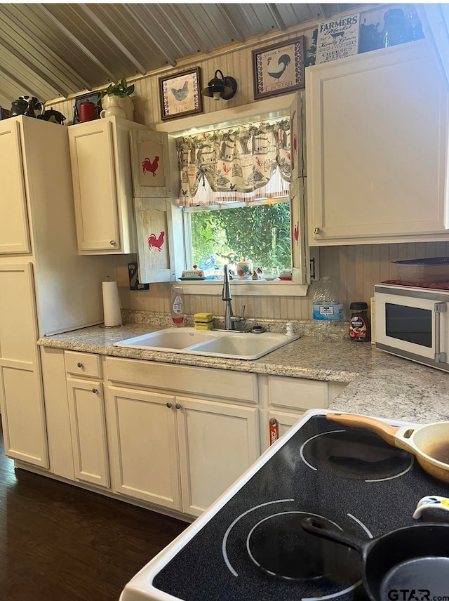 kitchen with wooden ceiling, wood walls, sink, range, and white cabinets