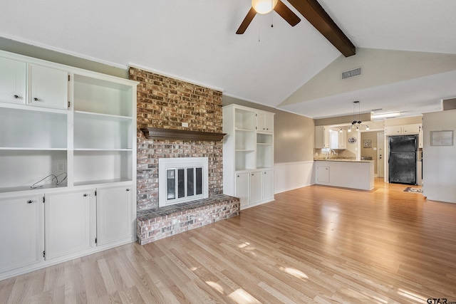 unfurnished living room featuring vaulted ceiling with beams, sink, ceiling fan, a fireplace, and light hardwood / wood-style flooring