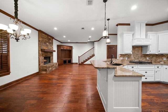 kitchen with white cabinets, sink, hanging light fixtures, a fireplace, and light stone counters