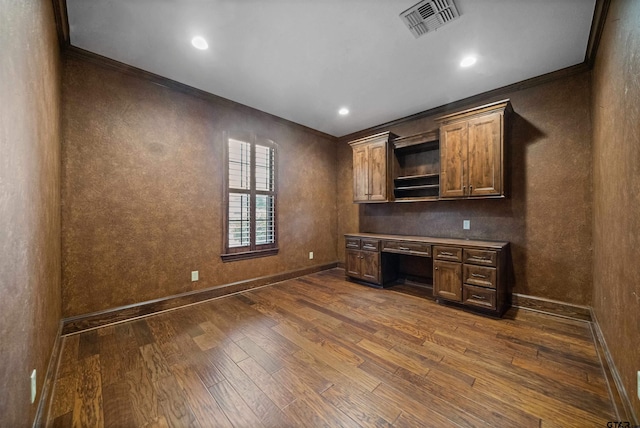 unfurnished office with crown molding, dark hardwood / wood-style flooring, and built in desk