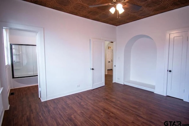 unfurnished bedroom featuring arched walkways, an ornate ceiling, baseboards, and wood finished floors