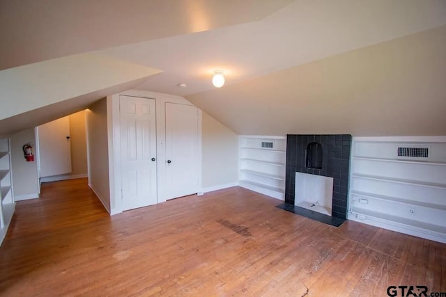 additional living space with visible vents, built in shelves, wood finished floors, and lofted ceiling