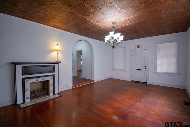 unfurnished living room featuring arched walkways, an ornate ceiling, wood finished floors, and a chandelier