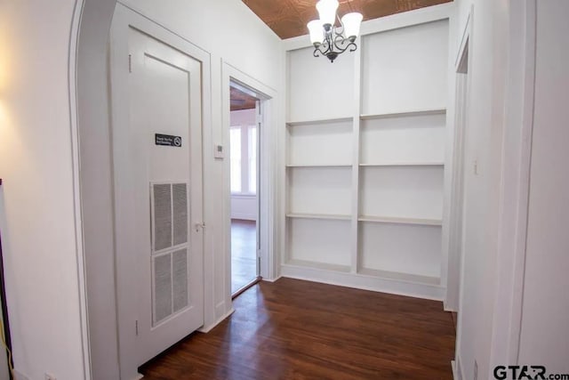 corridor featuring built in features, an ornate ceiling, a notable chandelier, and dark wood-type flooring