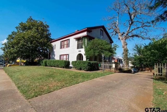 view of property exterior featuring a lawn, fence, stucco siding, and driveway