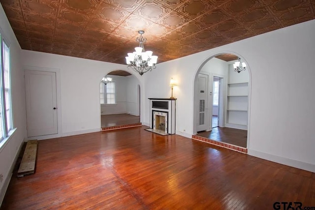unfurnished living room featuring arched walkways, an ornate ceiling, wood finished floors, and a notable chandelier