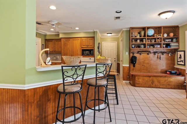 kitchen featuring kitchen peninsula, ornamental molding, a kitchen breakfast bar, ceiling fan, and black microwave