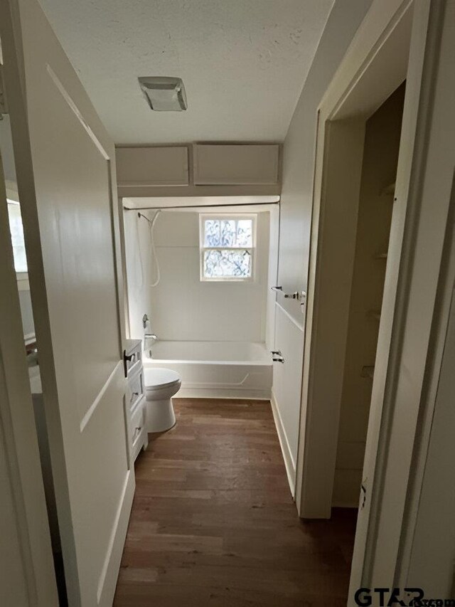 bathroom with shower / bathing tub combination, wood-type flooring, a textured ceiling, and toilet