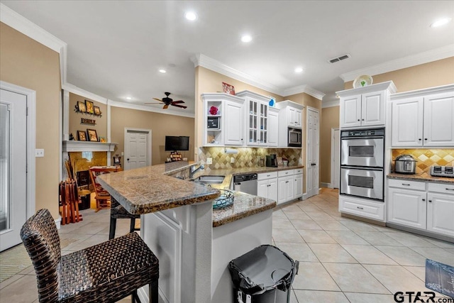 kitchen featuring a kitchen breakfast bar, tasteful backsplash, kitchen peninsula, white cabinets, and appliances with stainless steel finishes