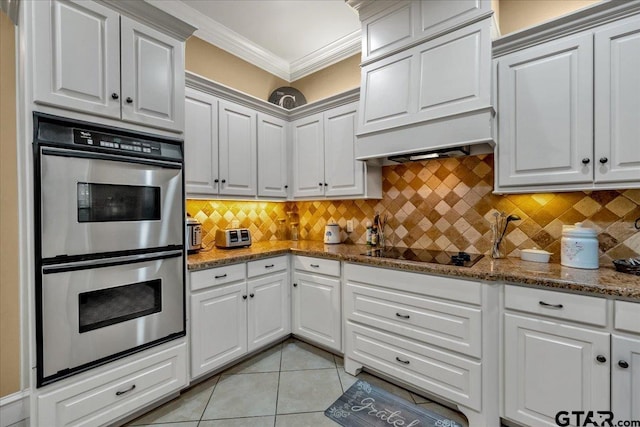 kitchen featuring stainless steel double oven, black electric cooktop, light tile patterned floors, dark stone countertops, and white cabinets