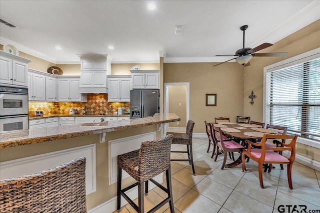 kitchen with refrigerator with ice dispenser, light stone countertops, white cabinetry, and double oven