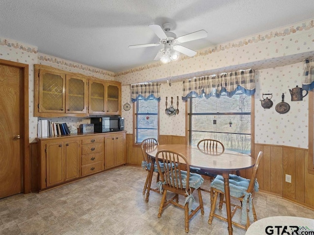564 County Road 1100, Daingerfield, TX 75638 - dining space featuring wallpapered walls, a wainscoted wall, a textured ceiling, wood walls, and a ceiling fan