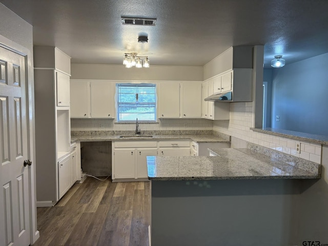 kitchen with light stone counters, a peninsula, dark wood-style flooring, a sink, and visible vents