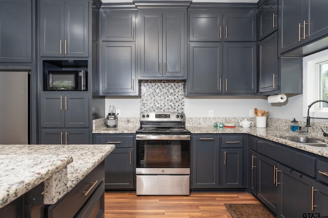 kitchen with sink, appliances with stainless steel finishes, light stone countertops, backsplash, and light hardwood / wood-style flooring